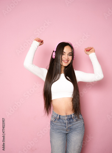 Young happy fun latin woman wear casual clothes and headphones listen to music dance gesticulating hands isolated on pink background studio portrait. Lifestyle concept photo