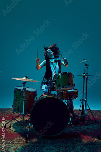 Artistic  expressive young woman  musician playing drums against cyan background in neon light. Concept of music  talent show  performance  concert  festival  instruments