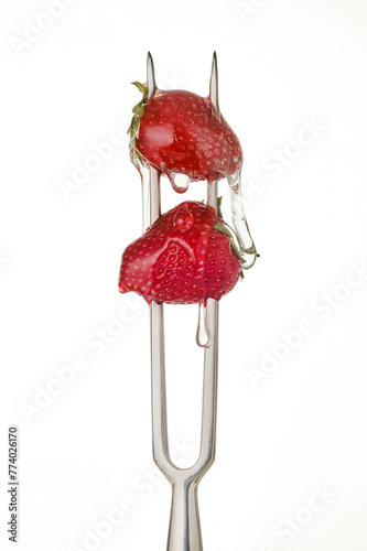 Strawberries pierced on a large fork with flowing clear sugar syrup  on a white background. Sugary sweetness. Selective focus