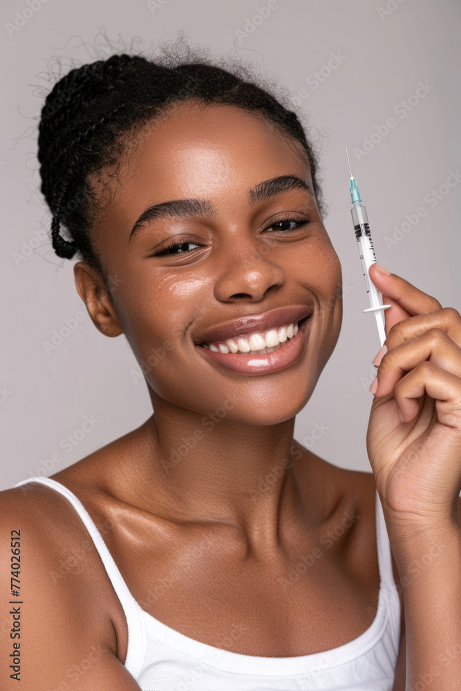 Smiling African American girl with a syringe in her hand on a plain background. Skin care. Spa day. Vertical orientation. Smiling African American girl with a syringe in her hand on a plain background. Skin care. Spa day. Vertical orientation.