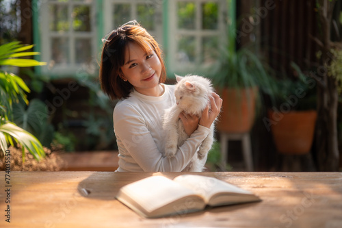 A woman shares a tender moment with her fluffy cat during a break from reading a book in a cozy outdoor garden setting. 