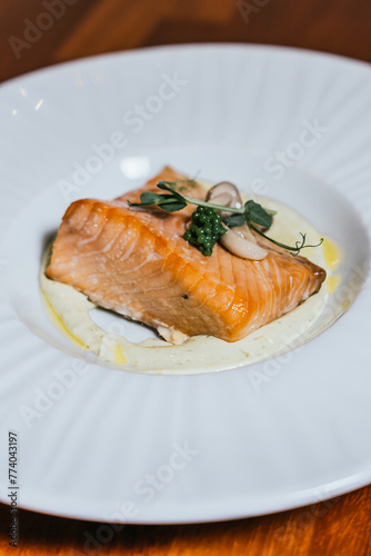 A beautifully poached salmon fillet rests on a creamy base, elegantly topped with caviar and fresh herbs on a white plate photo