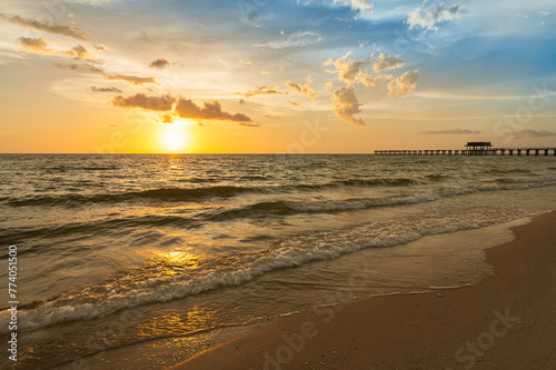 Sandy beach with rolling waves and a distant pier at sunset. Naples Beach, Florida