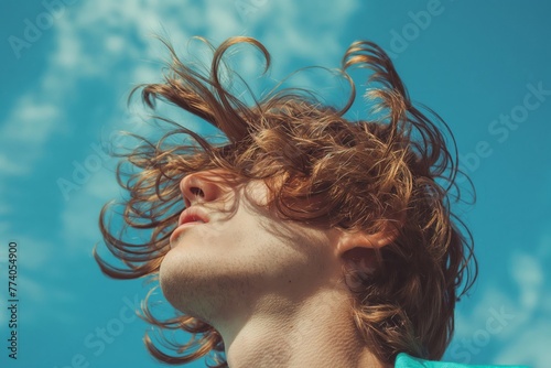 Dynamic low-angle shot capturing a man's shaggy hairstyle tossed by the wind under a clear blue sky photo
