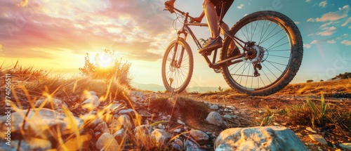 A cyclist rides a mountain bike on a rocky trail at sunrise from a low angle.
