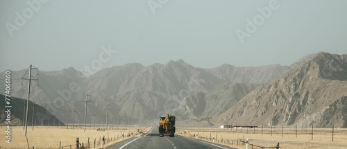 Image of a single tractor on the road in the middle of the yellow field and mountains. photo