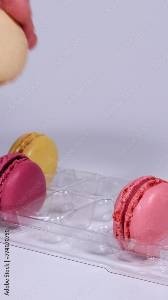 Slow motion of male and female hands putting fresh macaron cookies piece by piece in a transparent plastic box. Traditional french desserts from almond dough against white background. Slow motion of male and female hands putting fresh macaron cookies piece by piece in a transparent plastic box. Traditional french desserts from almond dough against white background.