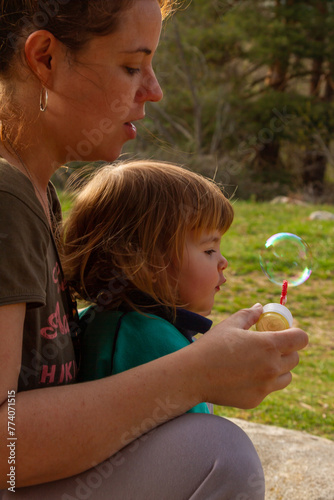 A pretty young woman plays with her two-year-old daughter to blow soap bubbles on a sunny day 