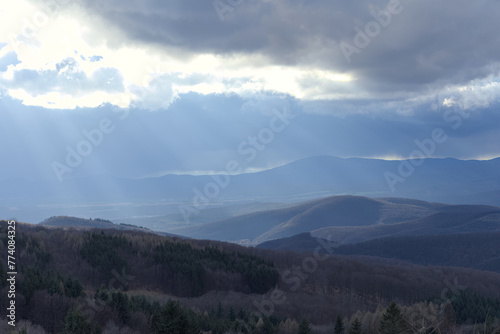 the sun's rays shine through the clouds on the hills behind them