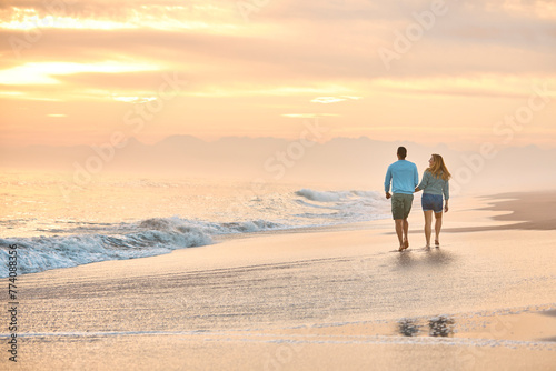 Rear View Of Couple In Casual Clothing On Vacation Holding Hands Walking Along Beach Shore At Dawn