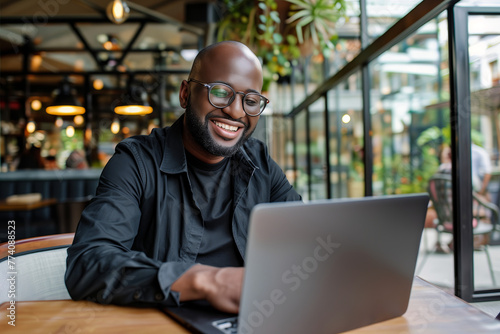 Happy man working online at a modern cafe with laptop