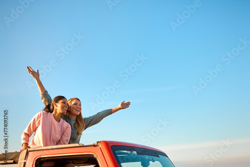 Couple With Friends On Vacation Driving Car On Road Trip Adventure To Beach Standing Up Through Roof