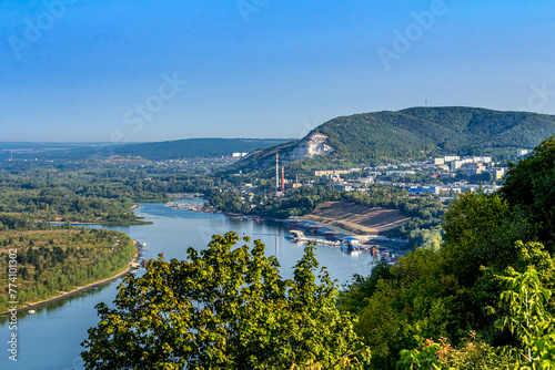A plant or factory on the banks of the Volga near the city of Samara, Russia against the backdrop of the Zhiguli mountains. Blue water, tree crowns, forest. Quiet summer morning with light sky. photo