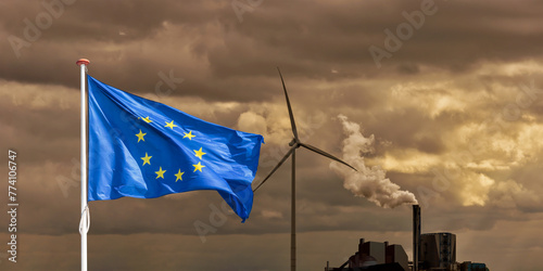 Waving European flag in front of a polluting factory chimney with smoke and wind turbine