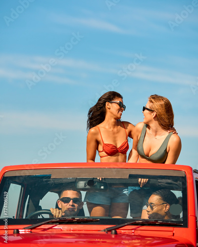 Couple With Friends On Vacation Driving Car On Road Trip Adventure To Beach With Women Standing © Monkey Business