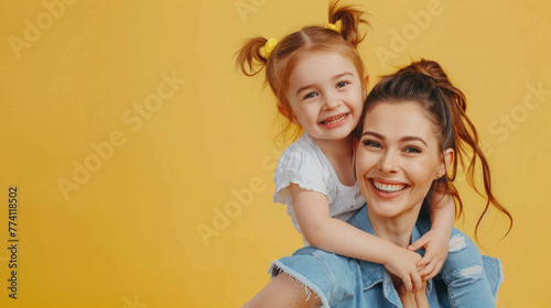 Cute little daughter in a white top and jeans with mom isolated on a yellow background in a studio portrait