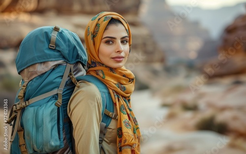 A woman wearing a scarf and a backpack is standing in a desert. She looks happy and confident