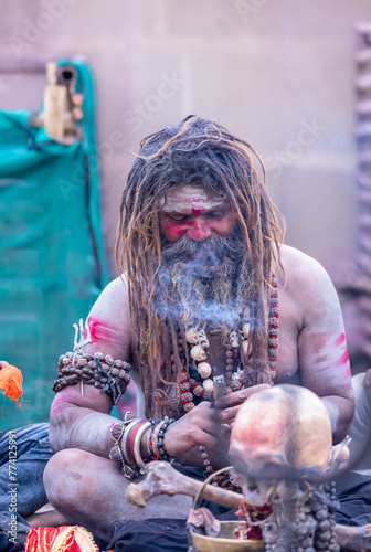 Portrait of an naga aghori sadhu holy man with pyre ash on his face and body smoking chilam at harishchandra ghat in varanasi.	 photo