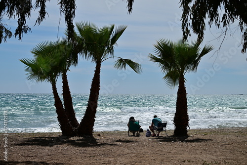 An elder love couple relaxing under palms at the beach of Benidorm-Spain on a warm April day.