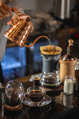 drip coffee, Barista making drip coffee by pouring spills hot water on coffee ground with prepare filter from copper pot to glass transparent chrome drip maker on wooden table in cafe shop