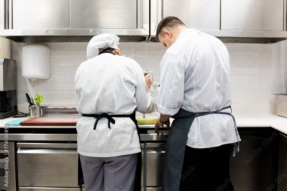 A couple of unrecognizable chefs are preparing a succulent menu in a restaurant kitchen.The woman is whipping a sauce while the man learns.Concept of fellow helpers in the kitchen.