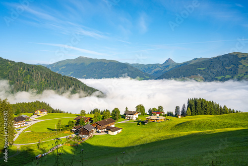 Morning clouds blanket the valley below a serene alpine landscape in Kitzbueheler Alps, with chalets and mountain peaks in view. Austria photo