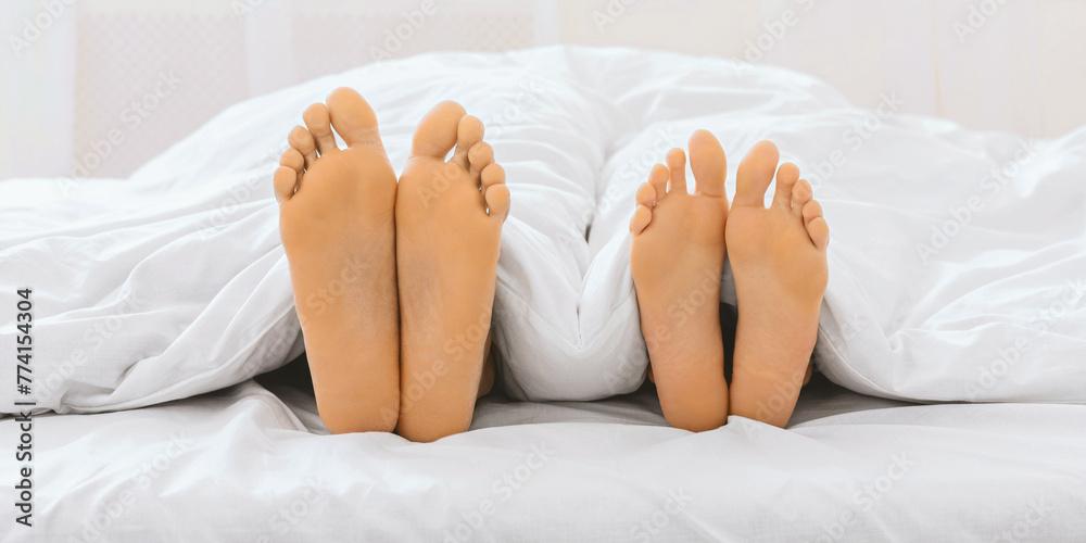 Two pairs of feet with painted toenails on bed sheets Two pairs of feet with painted toenails on bed sheets