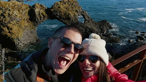 Romantic couple making selfie on tourist visit of Gatklettur Hellnar Arch, a stunning rock arch and basalt coastline at Arnarstapi, Snæfellsnes peninsula, Iceland. photo