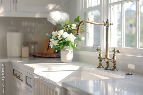 A gold kitchen faucet detail with an apron sink, white marble countertop and cabinets, and decorations in the background.