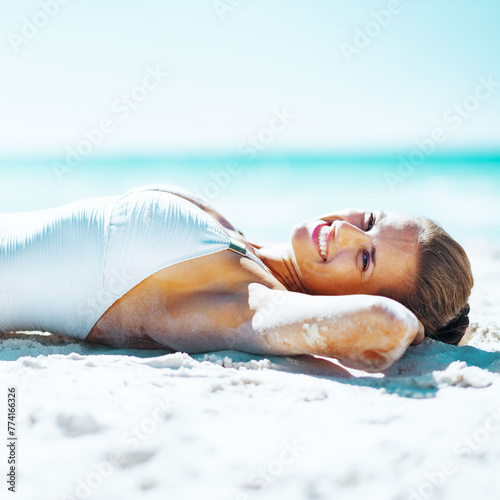 Happy young woman in swimsuit sunbathing on sandy beach