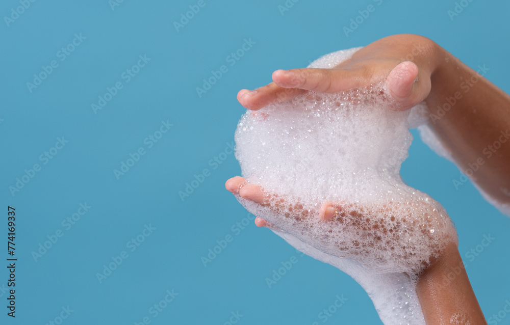 Fototapeta premium Female hand with soap bubbles on blue background. Hands with white bubbles.