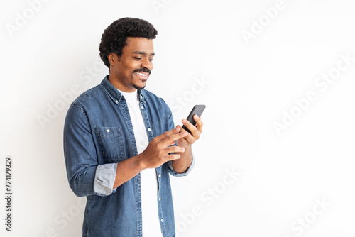 Joyful young black man in denim engaging with smartphone