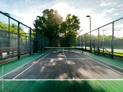 Summertime scene of elevated sport courts with nets in a public park setting. Courts are used for paddle tennis or pickleball play. Floor surface is green and blue with white boundary lines. photo
