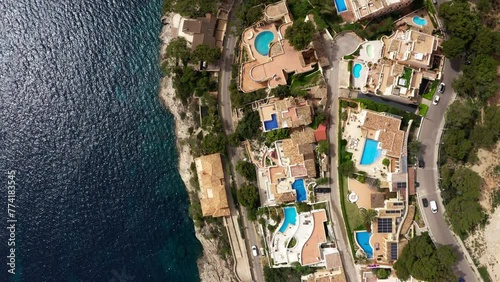 Beautiful aerial flying drone 4K video of Peguera town hotels, houses with tile roofs, swimming pools on rocky Mediterranean waves coastal town with narrow streets. Traveling and vacation concept photo