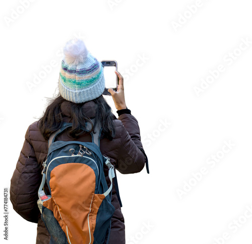 woman hiker brunette with long hair dressed in puffy jacket and winter hat with backpack on taking a photo on her mobile smartphone (cut out, isolated on white background)
