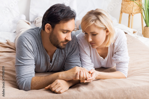 Image of closed eyes, leaned heads, holding hands man and woman, married couple, lay at bedroom, praying together before going to bed. Waiting child, pregnancy, problem issues, humility, plea concept. © vgstudio