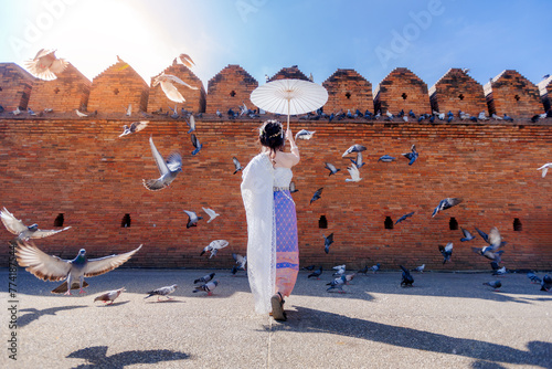 tourist woman wearing beautiful thai dress with white paper umbrella standing at Tha Phae gate among  flying pigeons, Chiang mai