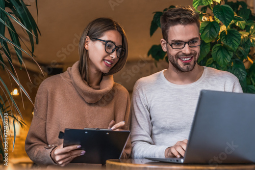 Two young business people working on laptop in coffee shop. Smiling young entrepreneurs working together in a cafe, coworking, . Caucasian colleagues discussing project in a modern worksplace photo