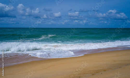 Tranquil scene of waves crashing on a sandy beach under a cloud-dotted sky