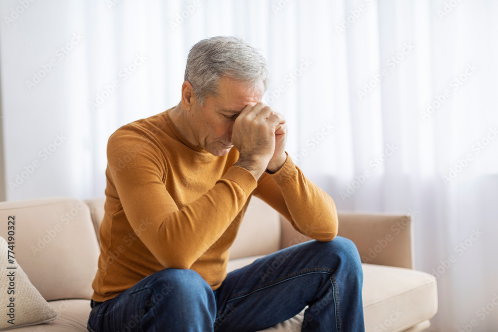 Elderly man sitting on sofa with head resting on hand Elderly man sitting on sofa with head resting on hand