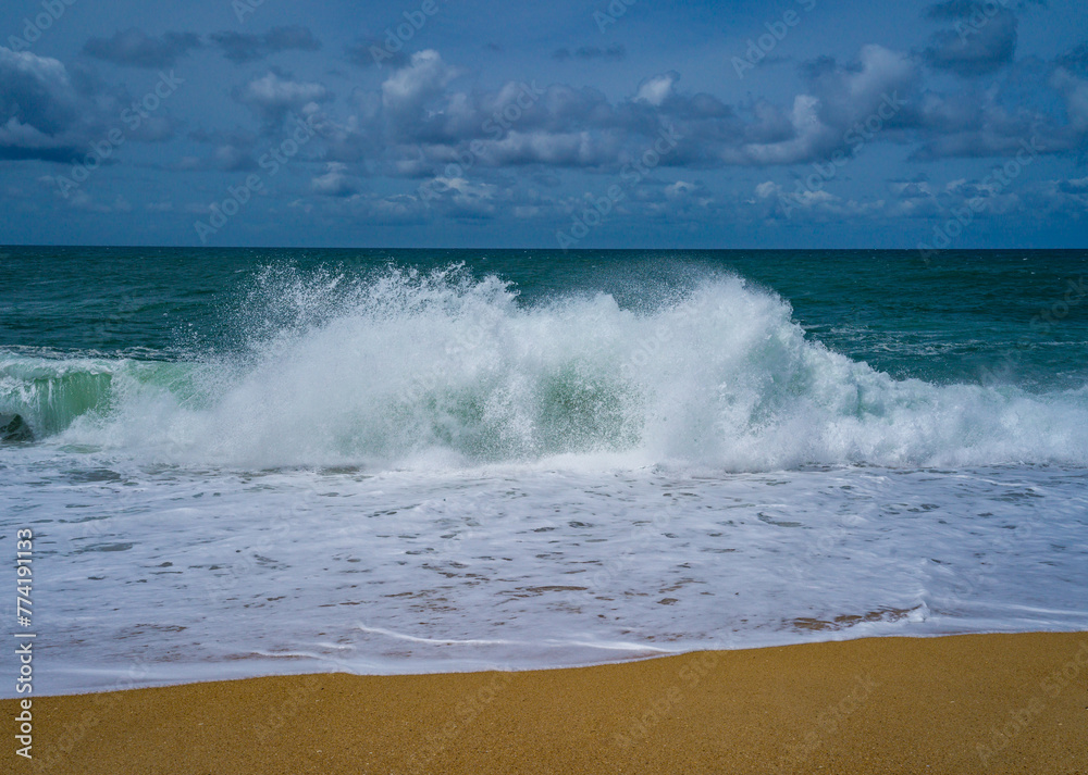 Tranquil scene of waves crashing on a sandy beach under a cloud-dotted sky
