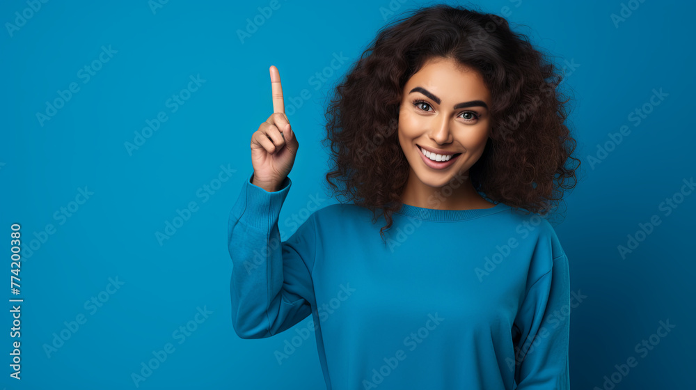 Portrait of young happy woman raising index finger on copy space for your ad on blue isolated background with copy space. Advertisement concept Portrait of young happy woman raising index finger on copy space for your ad on blue isolated background with copy space. Advertisement concept