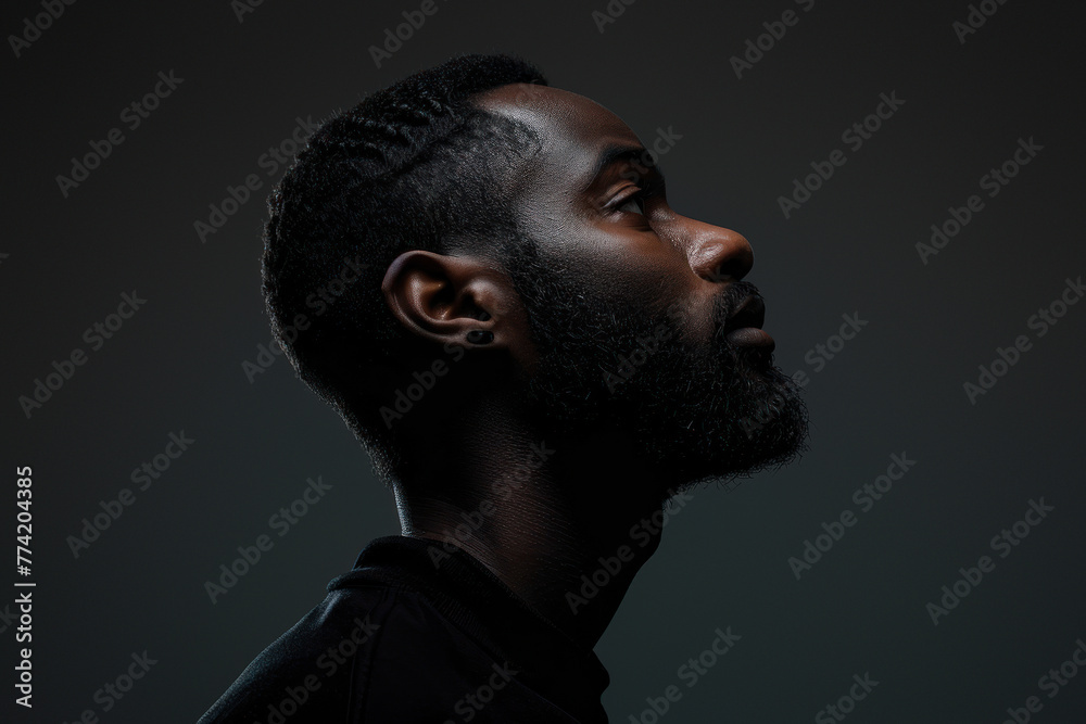 The image captures a side profile of an African man with a modern hairstyle against a dark background, giving it a moody feel The image captures a side profile of an African man with a modern hairstyle against a dark background, giving it a moody feel
