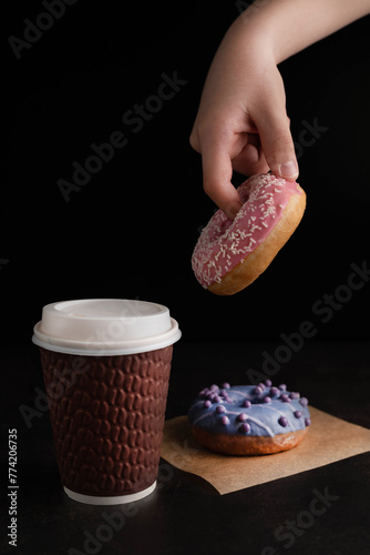 On a dark background, a glass of coffee, a hand holding a donut.
