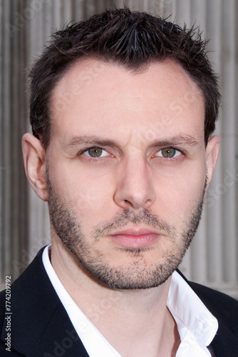 Portrait of man in mid 30's wearing white collar shirt and suit jacket against grey corrugated background 