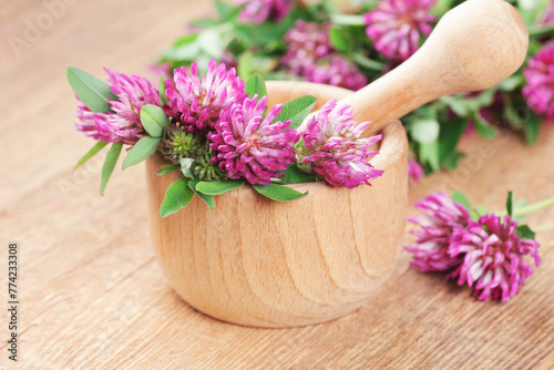 Red clover leaves or extract in wooden mortar with leaves and flowers on wooden table, closeup, remedy for menopause, source of estrogen, used in cosmetics, spa, face and hair beauty