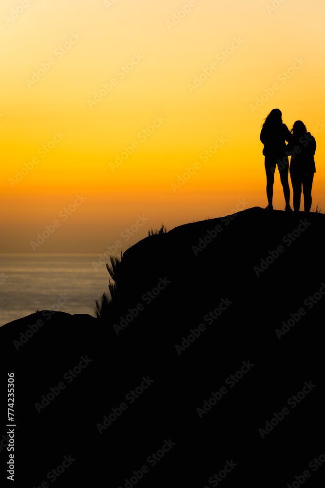 Silhouette of two girls watching the sunset together on the seashore