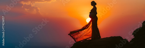 an indian mother drapped in a saree carrying her pregnancy standing on top of a cliff mountain silhouette shot sunset evening photo