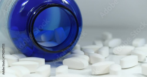 Big white pills scattered on table. Overdose. Open blue container for nutritional supplements lies on table. In reality these are biologically active sulfur pills in dosage of 1500 mg, MSM for joints photo