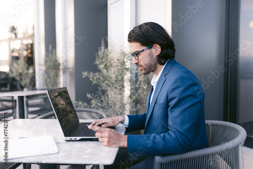 Side view of Serious Businessman Working on Laptop at Outdoor Cafe Table